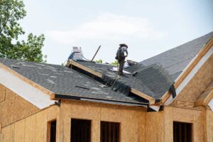 Adult using a secured ladder to attach outdoor lights along a gutter while another person steadies the ladder.