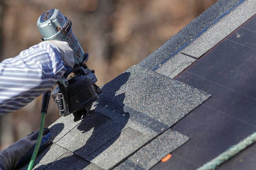 Homeowner inspecting roof shingles with binoculars while standing beside a ladder and gutter tools.