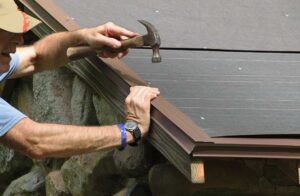 Person inspecting a leaf-covered roof edge beside clean gutters and autumn trees