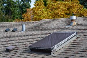 House with asphalt shingles and metal roof samples displayed on a workbench beside winter roofing tools.