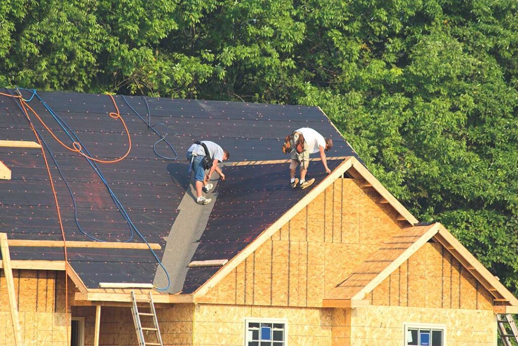 A homeowner examines new roofing materials beside a house with a clean, recently completed roof.