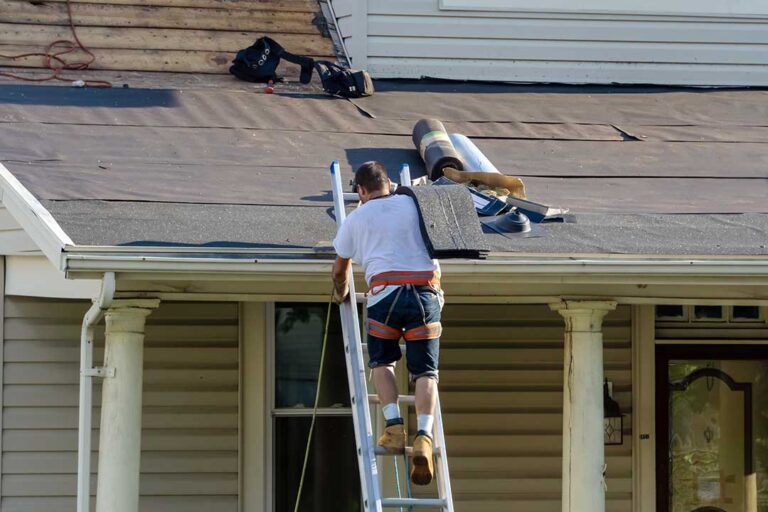 Homeowner inspecting roof shingles and clean gutters from a ladder beside a suburban house.