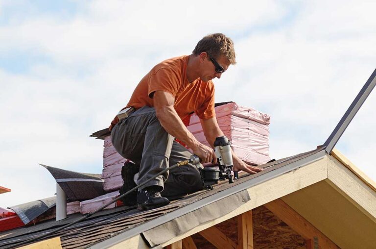 Roofing workers inspect exposed roof decking beside removed shingles on a residential home.