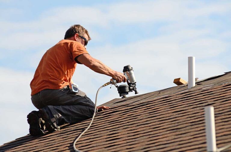 Homeowner reviewing roof plans beside a house while snow rests on the roof and gutters.