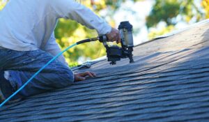 A homeowner reviews roof warranty papers beside a laptop, with inspection photos and roofing documents on a table.
